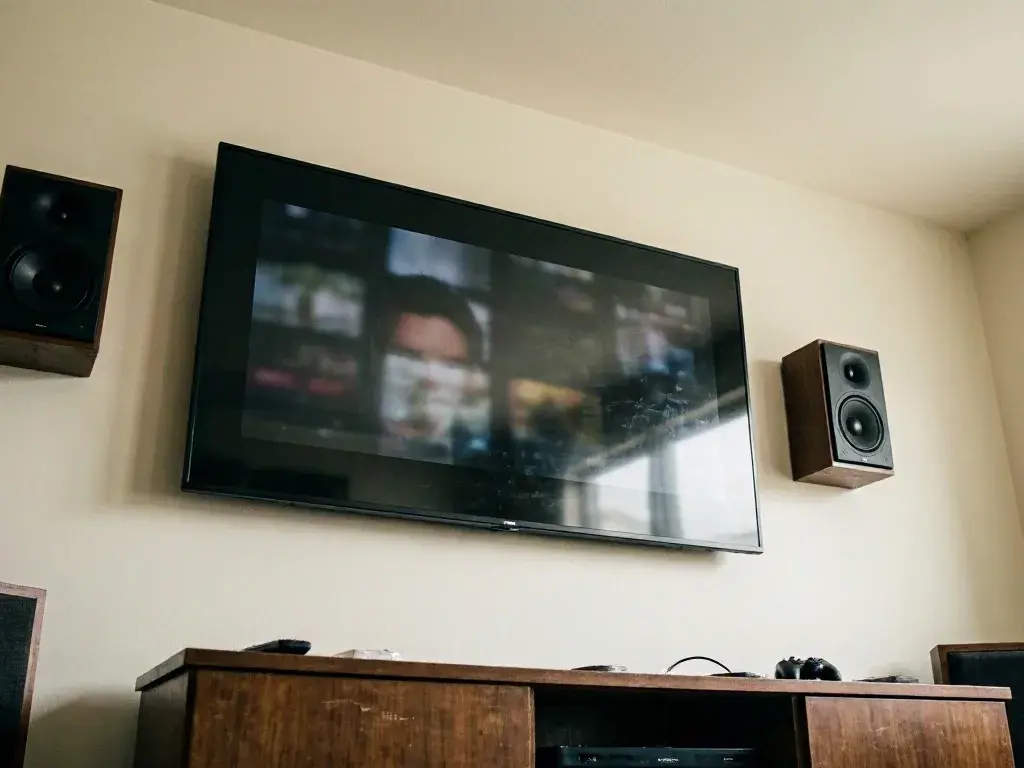 Wall-mounted television hangs between two speakers above a wooden console in a