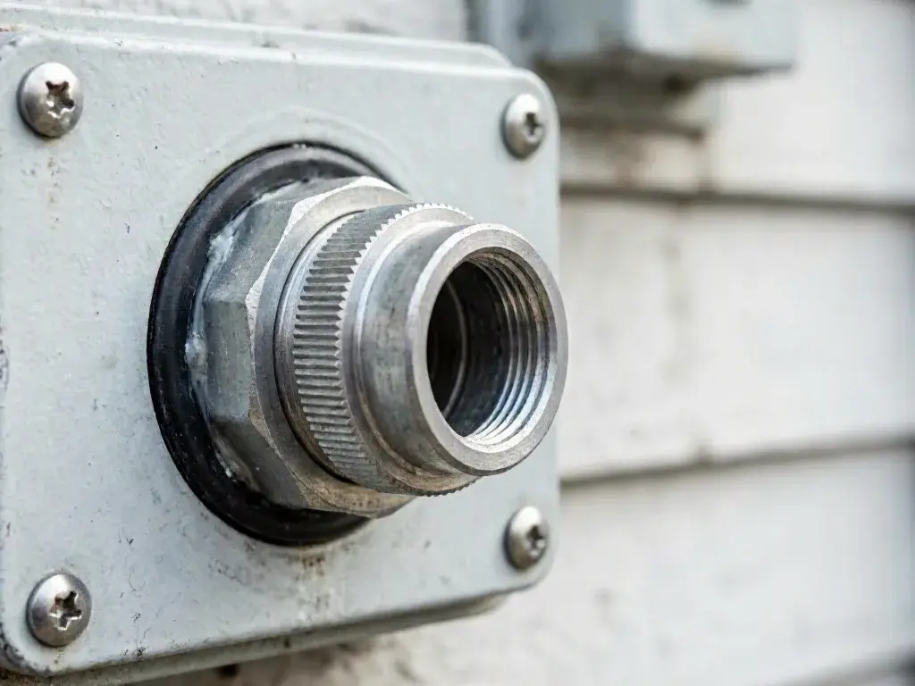 Close-up of a metal threaded pipe fitting mounted on a gray panel with screws