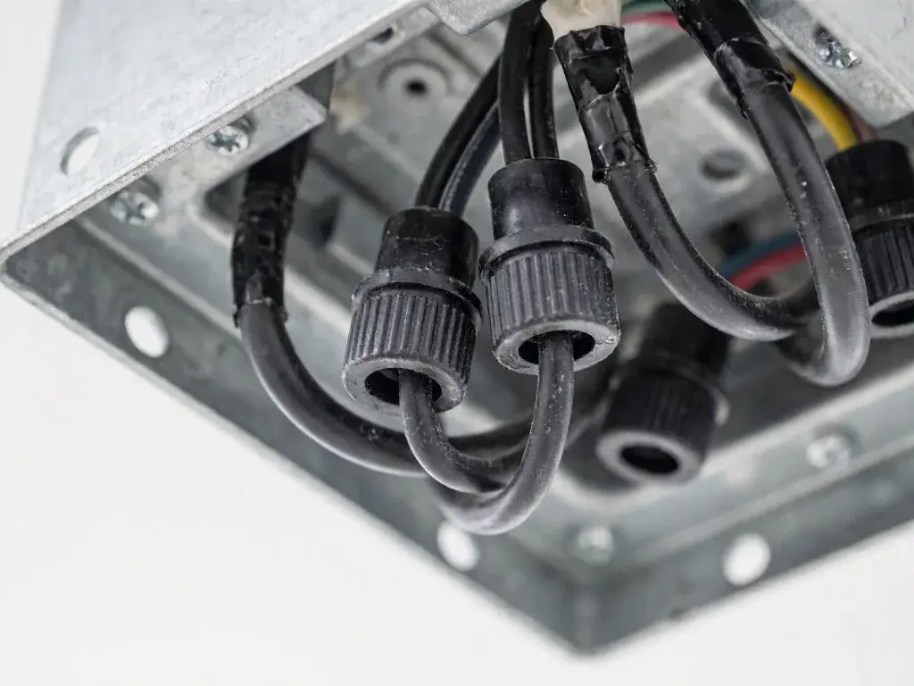 Black electrical cables enter a metal junction box with screw-on connectors