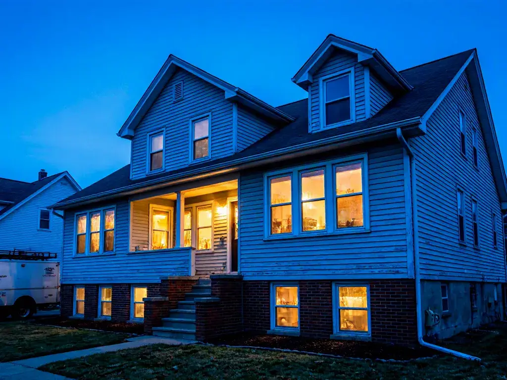 Two-story house with illuminated windows at dusk on a quiet residential lot
