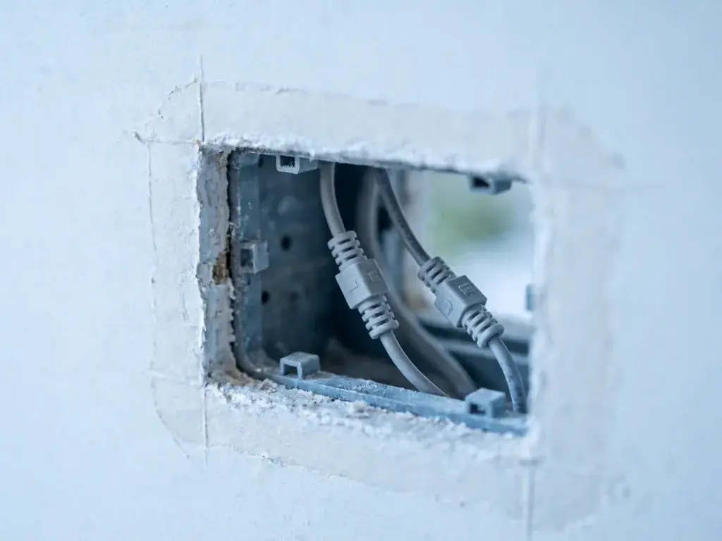 Wall opening exposing gray electrical cables inside a rough box surrounded by